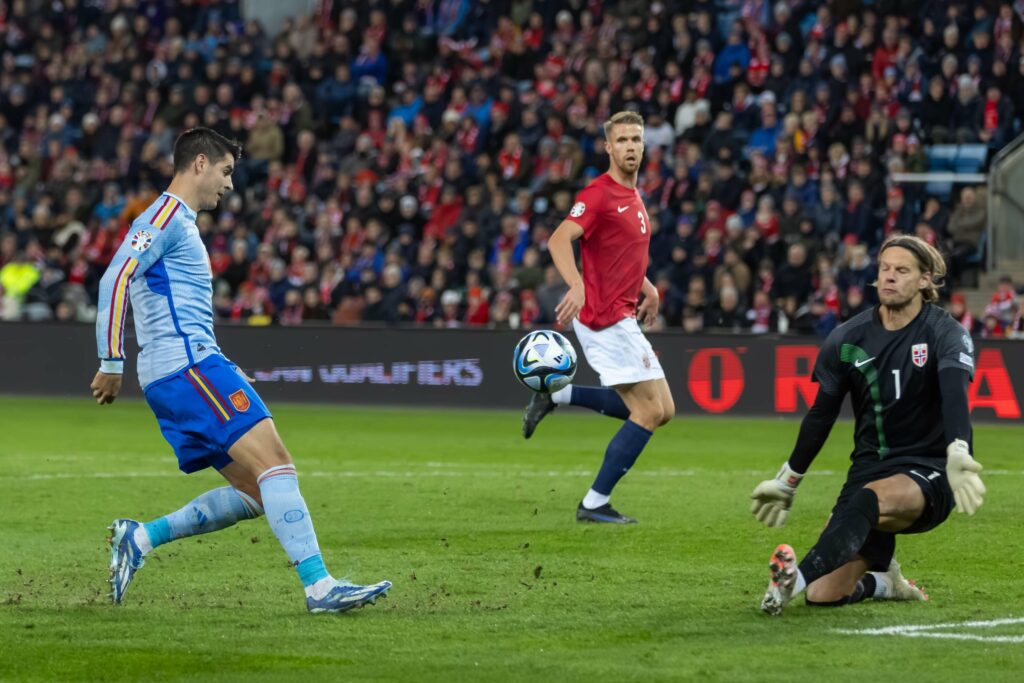 لاعب كرة قدم يرتدي زيًا أزرق فاتحًا وأحمرًا يستعد لتسديد الكرة نحو المرمى، بينما يحاول حارس المرمى الأسود صدها. وبينما يشاهد لاعب آخر يرتدي زيًا أحمر، يهتف مشجعو بيتواي أرابيا، ويملأون الاستاد بالطاقة الكهربائية.