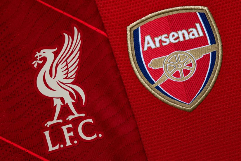 Gros plan de deux logos d'équipes de football sur tissu rouge. À gauche, l'emblème du Liverpool F.C. présente un oiseau blanc au-dessus de « L.F.C. » À droite, le logo d'Arsenal F.C., souvent vu dans les promotions de Betway Arabia, présente un canon sous son nom sur un badge rouge et bleu.