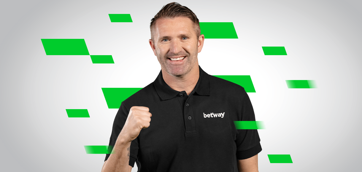 A man in a black polo shirt with the Betway Arabia logo smiles as he raises a fist. The background features gray tones accentuated by green geometric shapes, adding a dynamic flair to the scene.
