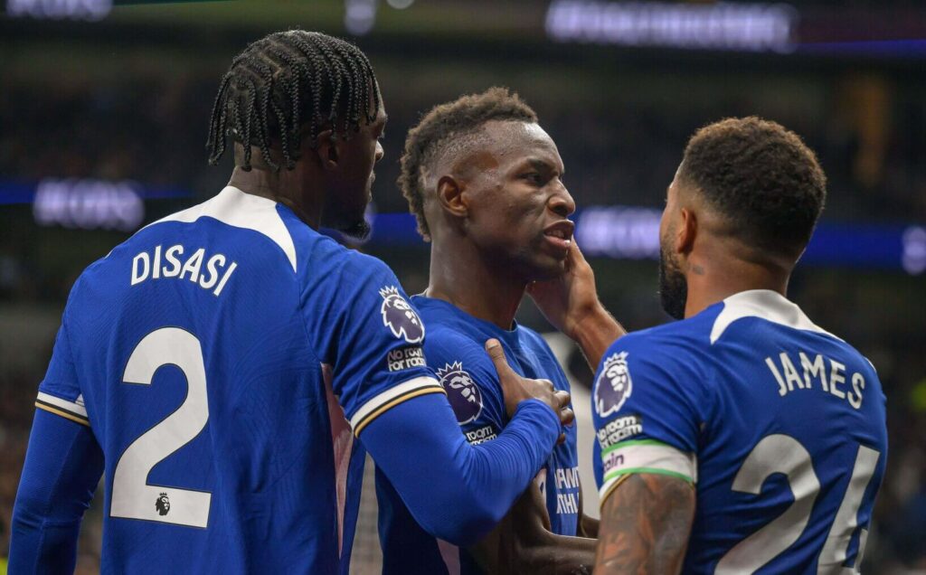 Three soccer players in blue jerseys stand on the field, sponsored by Betway Arabia. The center player is expressing intense emotion. Their jerseys display names and numbers two and twenty-four. In the blurred background, a vibrant stadium crowd cheers them on.