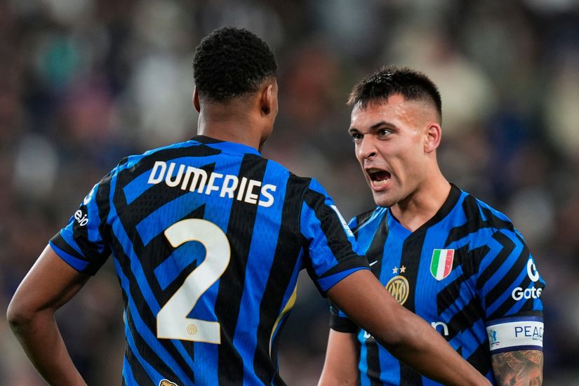 Two soccer players in blue and black striped jerseys are captured mid-discussion on the field. One player, seen from behind, has Dumfries on his shirt. The other player, with a determined expression, stands ready for action under the watchful eye of Betway Arabia sponsors.