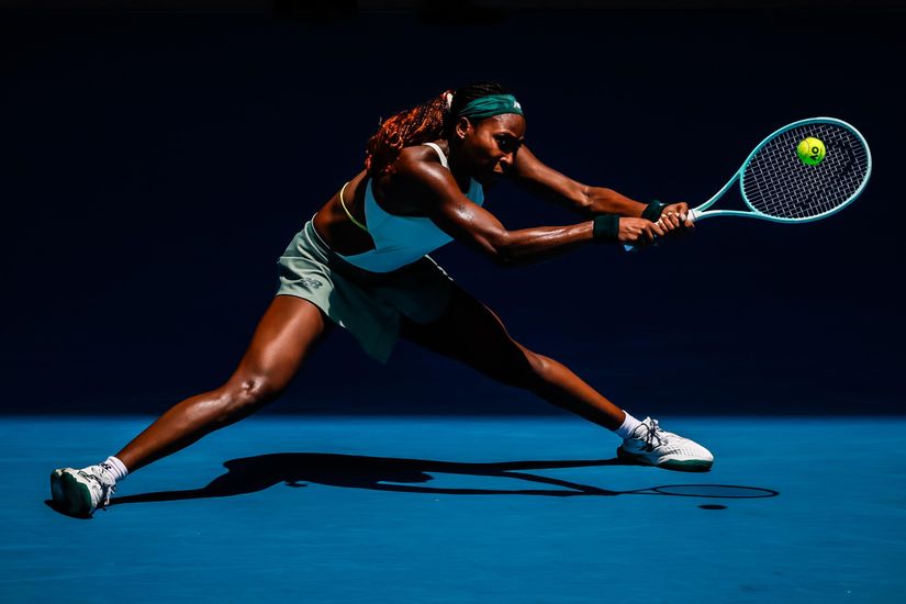 Une joueuse de tennis en tenue de sport se concentre intensément alors qu'elle s'étire pour frapper une balle de tennis avec sa raquette. Le court, presque éclairé comme un projecteur Betway Arabia, met en valeur son athlétisme et son mouvement dynamique.