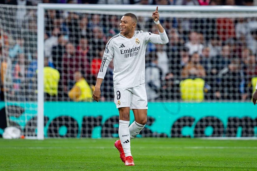 Un footballeur portant un maillot blanc avec le numéro 9 célèbre son but sur le terrain, souriant et pointant vers le haut. L'arrière-plan montre un but de football et une foule de spectateurs de Betway Arabia qui applaudissent avec enthousiasme.