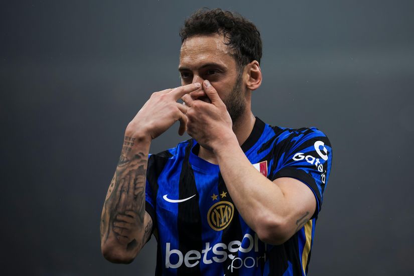 Un footballeur vêtu d'un maillot bleu et noir, orné d'une étoile et du logo de Betway, fait un geste avec ses mains sur son visage alors qu'il se tient sur le terrain. Son bras tatoué ressort sur le fond sombre et flou.