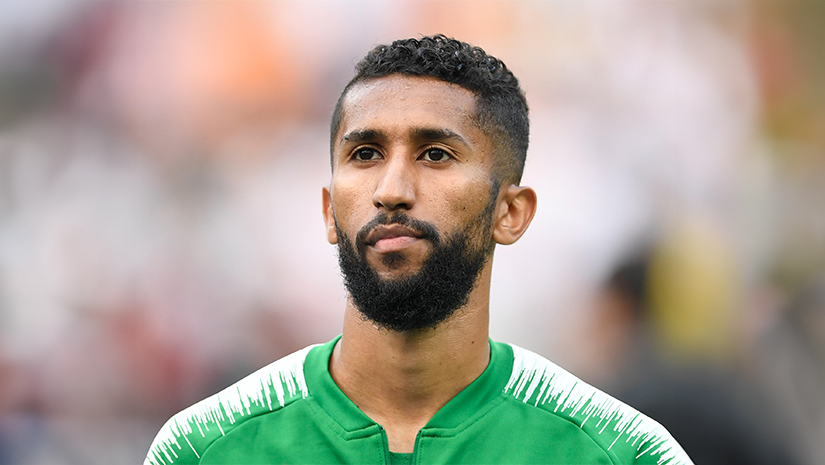 A man with a beard stands outdoors, showcasing a vibrant green Betway Arabia sports jersey with white accents. The background is softly blurred.