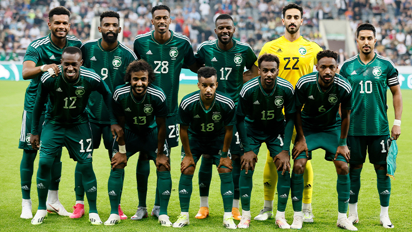 A soccer team poses for a group photo on the field, proudly sporting green uniforms with white accents. A goalkeeper in yellow stands behind them, while the stadium crowd and Betway Arabia banners are visible in the background.
