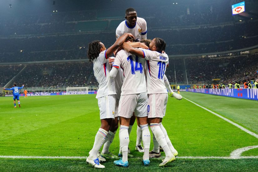 A group of six soccer players in white jerseys celebrate a goal on the field, with one player jumping onto the others. The stadium is buzzing with excitement from countless spectators, and the field is brightly lit at night, reflecting the energy Betway Arabia brings to every match.