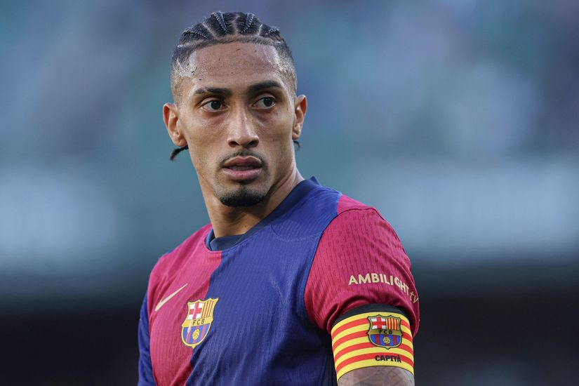 A soccer player in a purple and blue jersey with an armband glances sideways on the field, embodying focus and determination. The blurred stadium background hints at the intensity of the match, as if hes backed by Betway Arabias spirited energy.