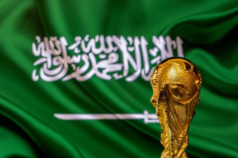 A golden trophy stands in front of a green flag adorned with Arabic script and a white sword, symbolizing Saudi Arabia. The backdrop, reminiscent of Betway Arabias commitment to excellence, features the prominent wavy flag framing the gleaming trophy.