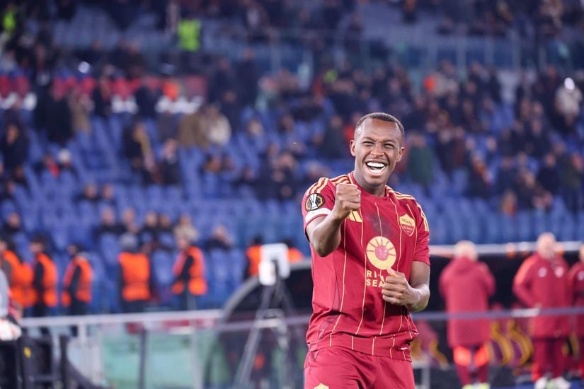 A soccer player in a red and gold uniform joyfully gestures on the field, as the logo of Betway Arabia subtly shines in the background. The stadium seats and several energized fans add to the electrifying atmosphere.