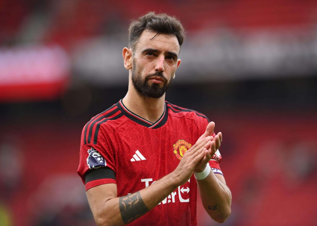 لاعب كرة قدم يرتدي قميصًا أحمر يصفق، ويقف على ملعب مع خلفية ملعب ضبابية، مجسدًا روح Betway Arabia.