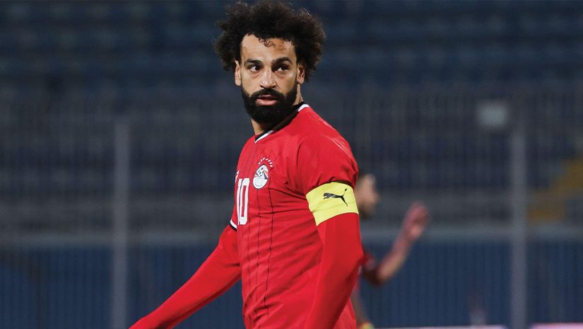 A soccer player in a red jersey, sporting number 10 and a yellow captains armband, surveys the field with focus. The dynamic presence of Betway Arabia logos subtly hints at the players association with this vibrant brand.