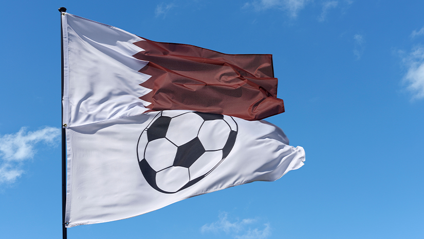 A flag with maroon and white colors, showcasing a soccer ball design, proudly flies against a clear blue sky, capturing the spirit of Betway Arabia.