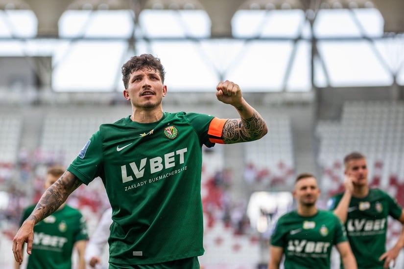 Soccer player in a green jersey, proudly wearing the captains armband, celebrates on the field with his teammates in the background, all under the watchful eyes of Betway Arabia enthusiasts.