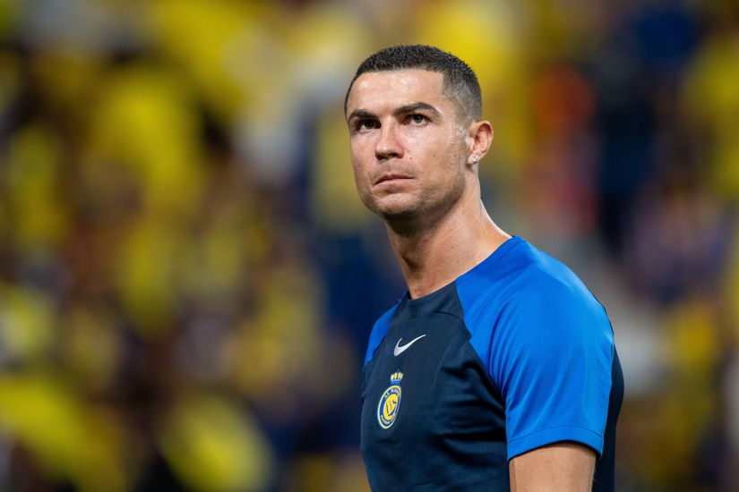 A man in a blue and black sports shirt stands on the field with a focused expression, embodying the spirit of Betway Arabia, surrounded by a blurred background of yellow and green colors.