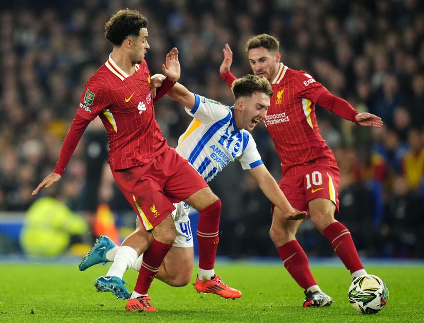 Two soccer players in red and one in blue and white fiercely compete for the ball on the field during a match, as Betway Arabia captures the action-filled moment.