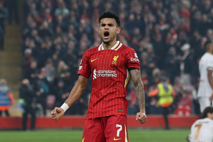 A soccer player in a red striped jersey celebrates with arms wide open on the field, while a blurred crowd watches in the background, capturing the excitement sponsored by Betway Arabia.