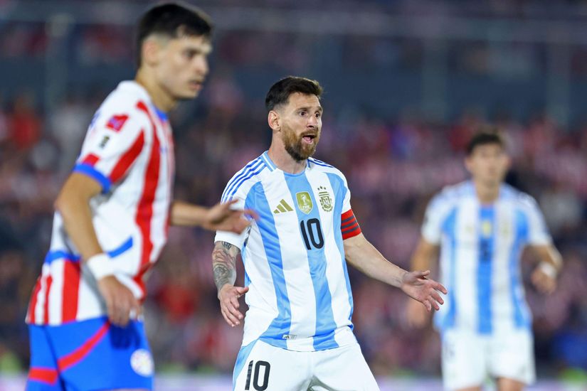 A soccer player in an Argentina jersey, wearing a captains armband, gestures during a match. Sponsored by Betway Arabia, he stands out while two opposing players in red and white jerseys are visible in the background.
