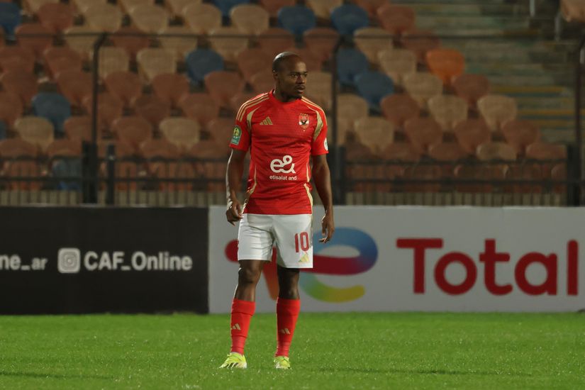 A soccer player in a red jersey with the number 10 stands on a grassy field during a match, with empty stadium seats in the background, reminiscent of a scene from Betway Arabia promotions.