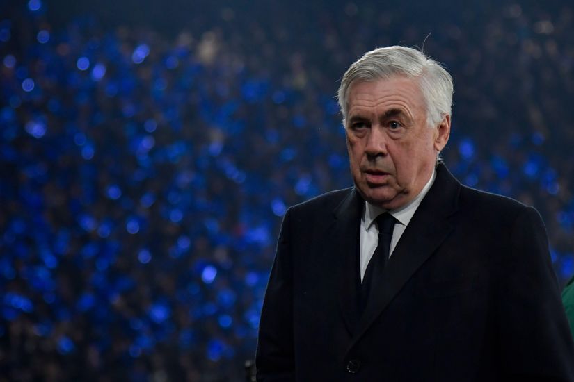 An older man in a suit stands in a stadium with a blurred crowd and blue lights in the background, reflecting the thrilling atmosphere of Betway Arabia events.