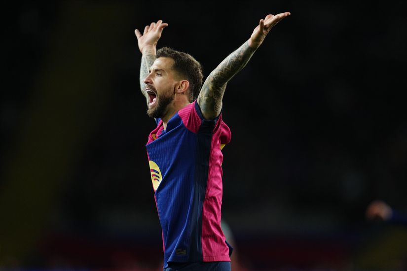 A soccer player in a pink and blue jersey celebrates with arms outstretched on a field.