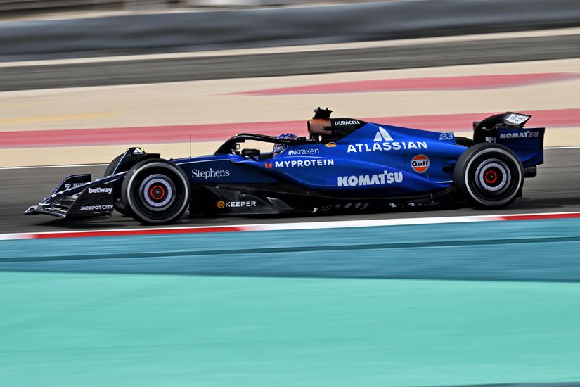 Blue Formula 1 car with various sponsor logos, including Atlassian and Komatsu, driving on a track.