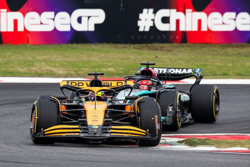 Two Formula 1 cars racing on a track, with a red and purple #ChineseGP banner in the background.