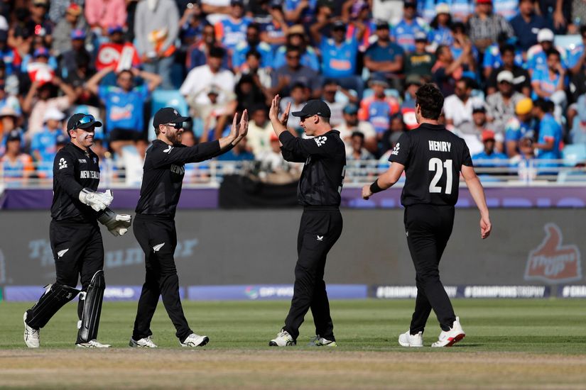Four New Zealand cricket players in black uniforms celebrate on the field; a crowd in the background watches.