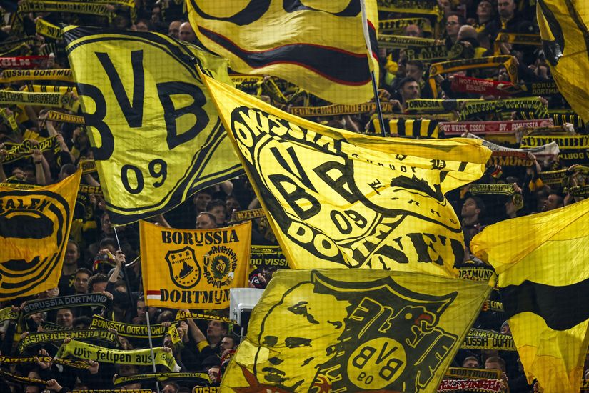 Fans waving large yellow and black Borussia Dortmund flags in a crowded stadium.