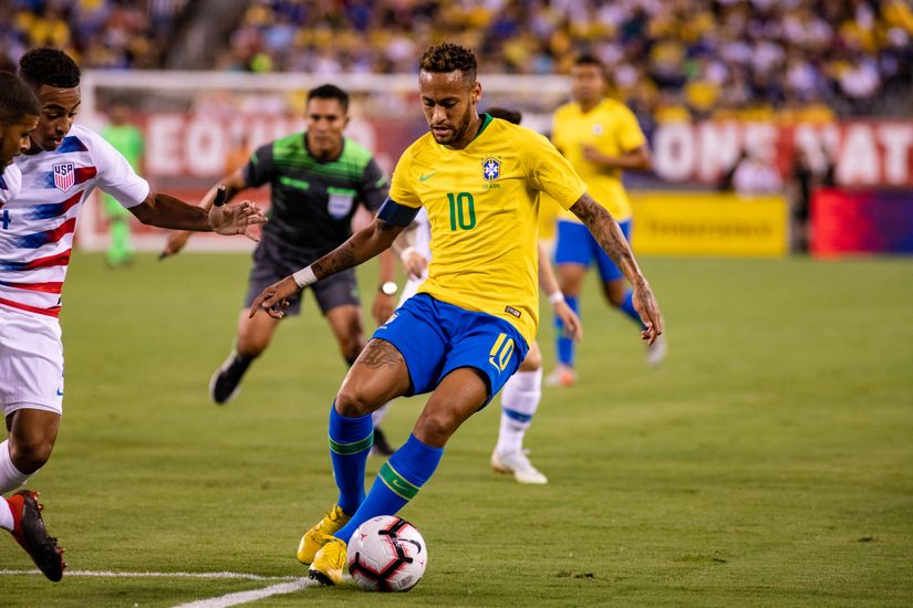 A soccer player in a yellow jersey dribbles the ball past opponents on a field during a match.