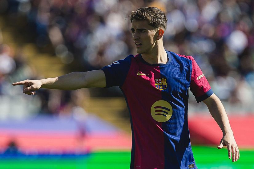 Soccer player in a blue and red jersey pointing, with a stadium crowd in the background.