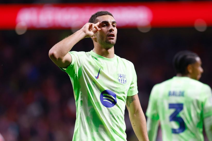 Soccer player in light green jersey gestures near his face on the field, with a teammate in the background.