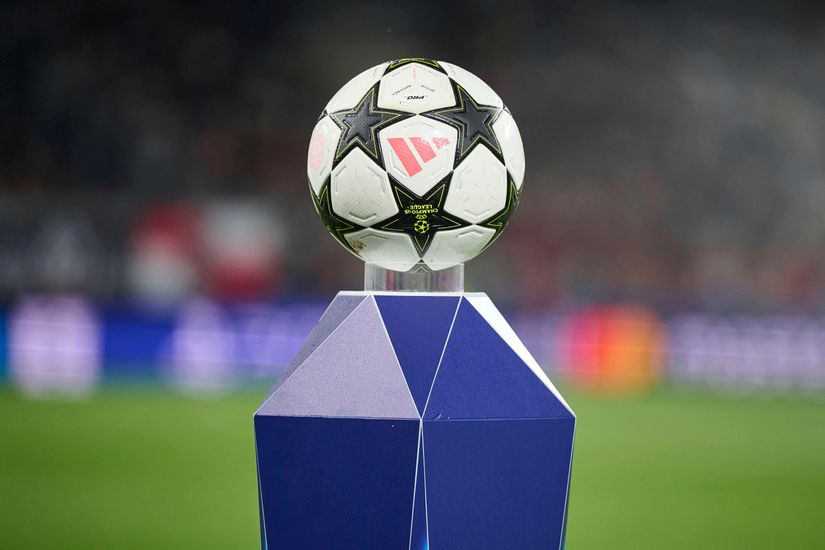 A soccer ball with a star pattern is displayed on a geometric pedestal, with a blurred stadium in the background.