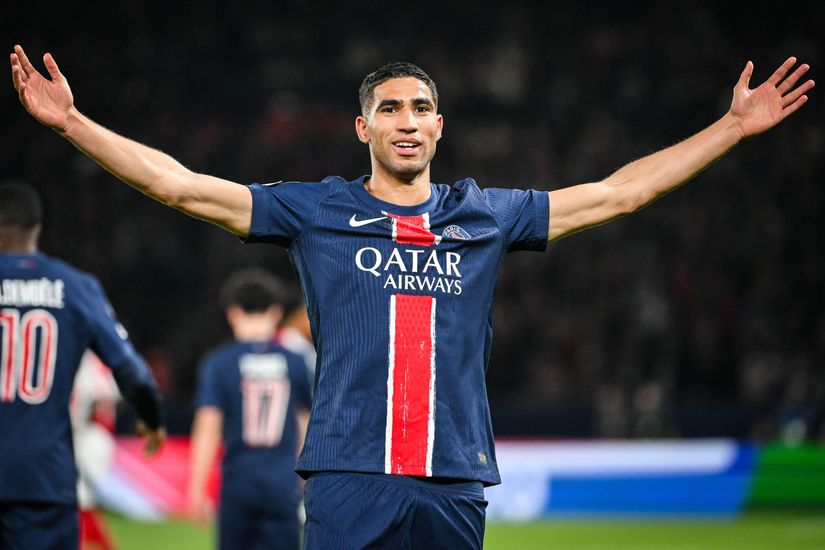 Soccer player wearing a PSG jersey stands on the field with arms outstretched during a match.