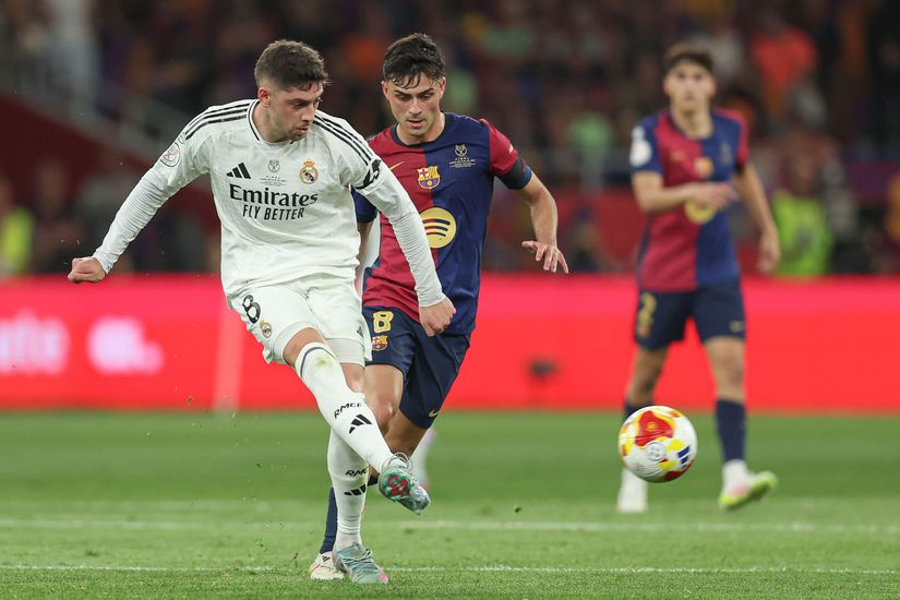A Real Madrid player kicks the ball while a Barcelona player defends during a soccer match on the field.
