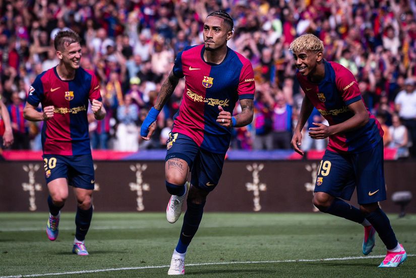 Three FC Barcelona players celebrate on the soccer field in front of a cheering crowd, all wearing the teams red and blue kits.