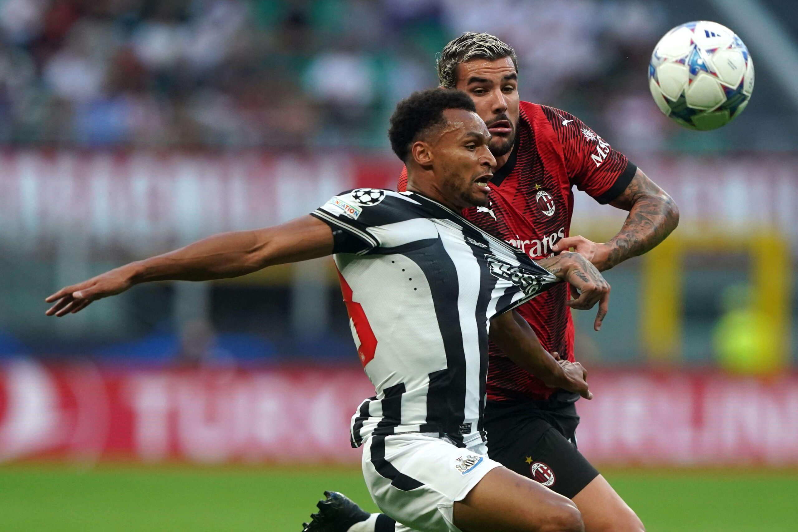 During the match, two soccer players vie for control. The player in black-and-white stripes uses his chest to reach for the ball as the one in red-and-black seeks to intercept. Amidst this dynamic scene, banners like Betway Arabia subtly color the blurred stadium backdrop.