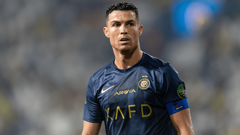 يقف لاعب كرة قدم يرتدي قميصًا أزرق داكنًا مكتوبًا عليه KAFD على المقدمة ويرتدي شارة القيادة بثقة على أرض الملعب، محاطًا بحشد من المتفرجين المتحمسين. يجسد المشهد روح Betway Arabia، التي توحد المشجعين من خلال شغفهم باللعبة.