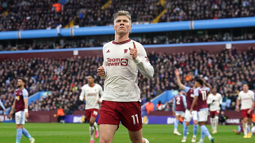 A soccer player in a white jersey with red shorts celebrates on the field, giving a thumbs-up gesture. Teammates and opponents in similar uniforms are visible in the background. The stands, buzzing with excitement, hint at the electrifying atmosphere of a Betway-supported match.