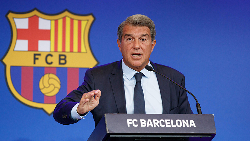 A man in a suit speaks at a podium with FC BARCELONA written on it. Behind him, the FC Barcelona crest shines against a blue background. As he gestures passionately to the audience, theres a hint of collaboration in the air, possibly pointing towards something exciting with Betway.