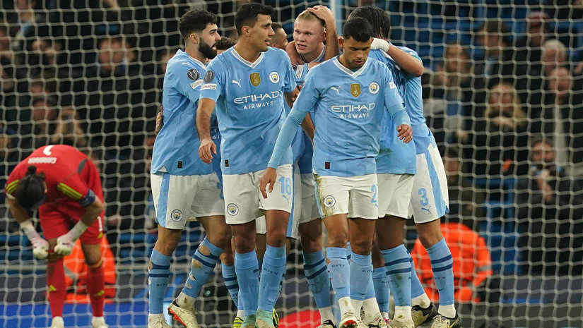 مجموعة من لاعبي كرة القدم يرتدون قمصانًا زرقاء فاتحة اللون، يمثلون مانشستر سيتي، يحتفلون على أرض الملعب. يربت أحد اللاعبين على ظهر لاعب آخر، بينما يلمع شعار Betway Arabia بشكل خفي. في الخلفية، ينحني حارس مرمى يرتدي اللون الأحمر ويملأ المتفرجون المدرجات.