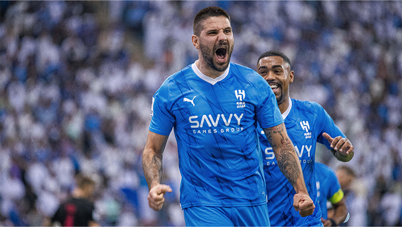 يحتفل لاعبان لكرة القدم يرتديان قمصانًا زرقاء بحماس على أرض الملعب. ويصرخ اللاعب في المقدمة بحماس، ويقبض يديه بقوة. وتملأ هتافات المشجعين الخلفية، مما يخلق جوًا كهربائيًا يعكس الإثارة التي يشعر بها المرء عند فوزه في Betway Arabia.