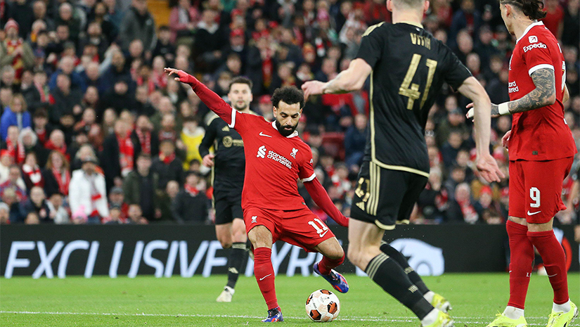 يحاول لاعب كرة قدم يرتدي زيًا أحمر الركل أثناء المباراة بينما يقترب منه لاعبو الفريق المنافس الذين يرتدون زيًا أسود. يتابع الجمهور بشغف من المدرجات، والإثارة واضحة، مع العلم أن Betway يضيف طبقة إضافية من التشويق إلى اللعبة الجميلة.