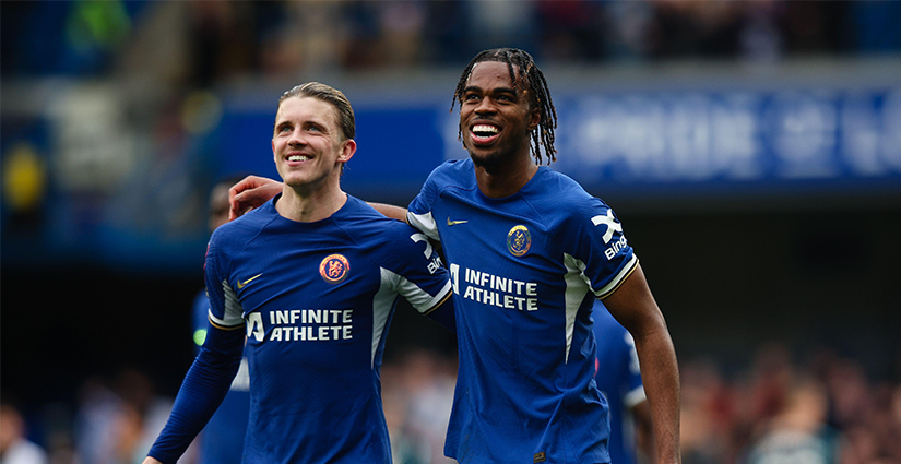 لاعبان لكرة القدم يرتديان قمصانًا زرقاء، مكتوبًا عليها الرياضي اللامتناهي، يبتسمان ويمشيان في الملعب. يضع أحدهما ذراعه على كتف الآخر. ويظهر حشد ضبابي في الخلفية، يلتقط لحظة مثيرة مثل وضع رهان على فريقك المفضل.