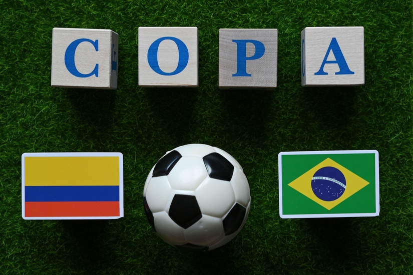 تستقر الكتل التي تحمل كلمة COPA على العشب، وتحيط بها أعلام كولومبيا والبرازيل النابضة بالحياة بجانب كرة القدم، مما يعكس روح اللعبة. استمتع بهذه اللحظة المثيرة مع Betway، حيث تشعر أن كل مباراة أقرب من بداية المباراة إلى الهدف.