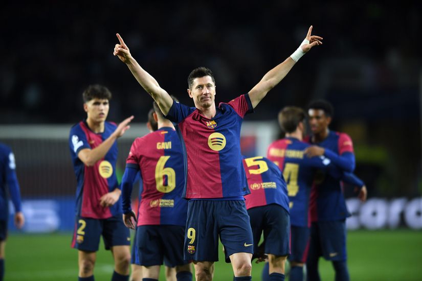 A soccer player wearing a blue and red jersey, numbered 9, raises both arms in celebration on the field. Sponsored by Betway Arabia, his teammates in similar jerseys are visible in the background, some with their backs turned.