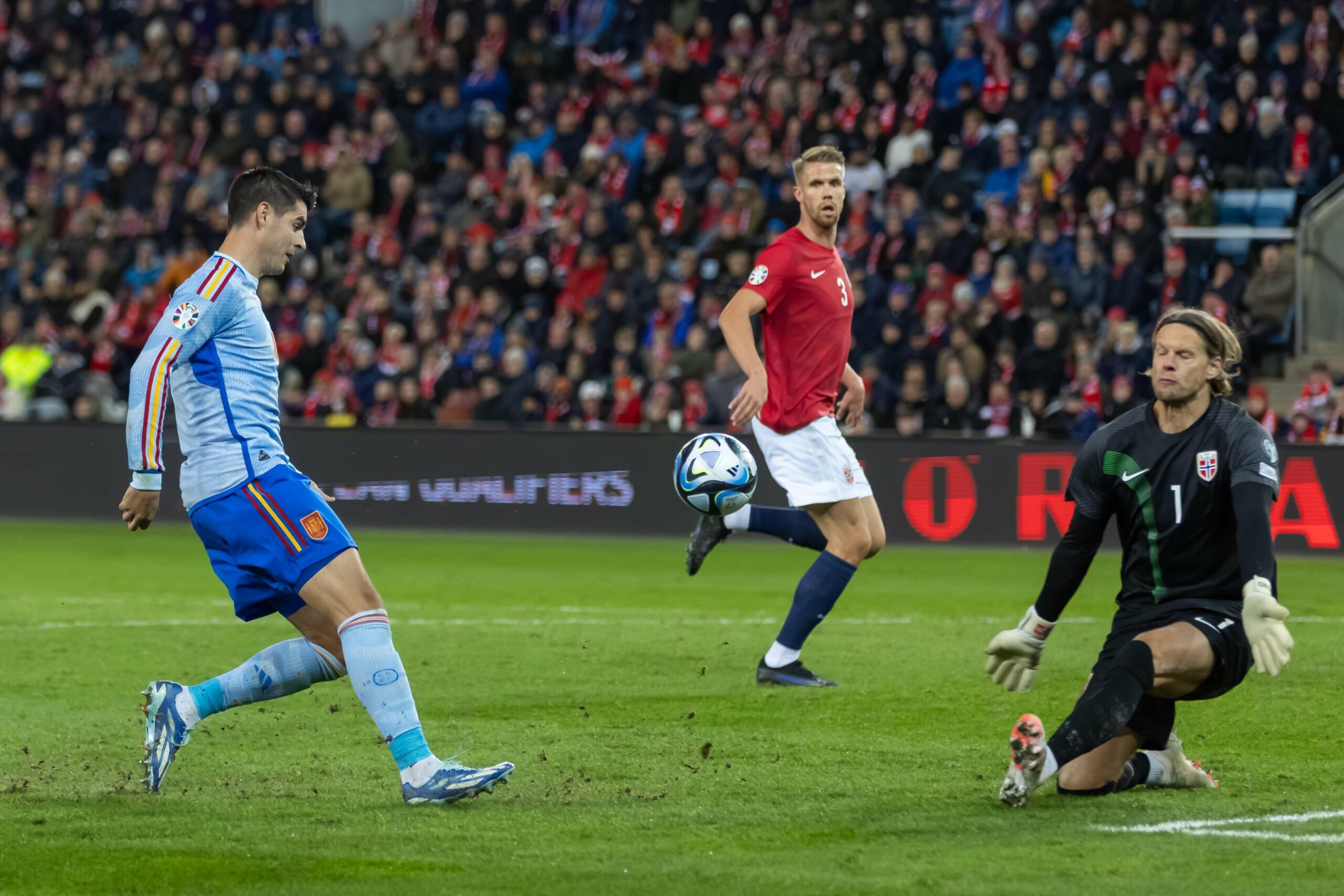 لاعب كرة قدم يرتدي زيًا أزرق وأبيض يسدد الكرة ببراعة أمام حارس مرمى يرتدي زيًا أسود خلال مباراة متوترة. وبينما تثير احتمالات Betway Arabia حماس الجماهير، يشاهد لاعب آخر يرتدي قميصًا أحمر من الخلفية بينما يمتلئ الاستاد بالإثارة.